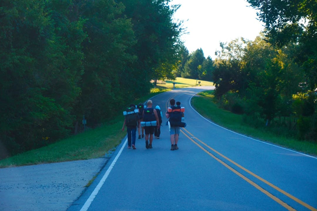 Friends walking a tree-lined road with backpacks