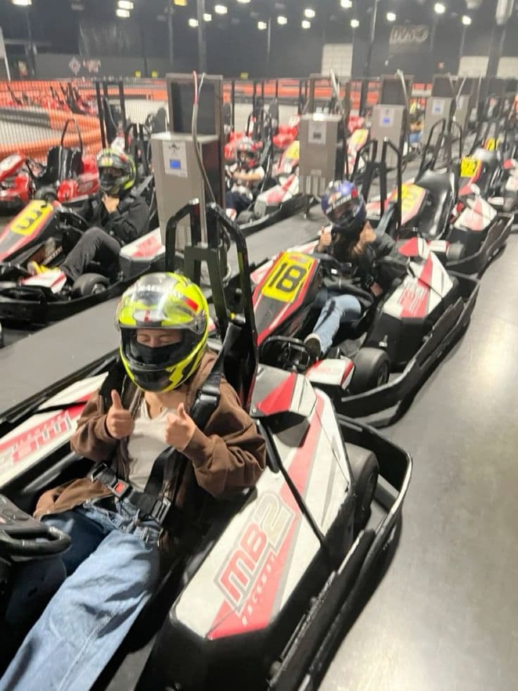 Friends in helmets sitting in go-karts giving a thumbs up